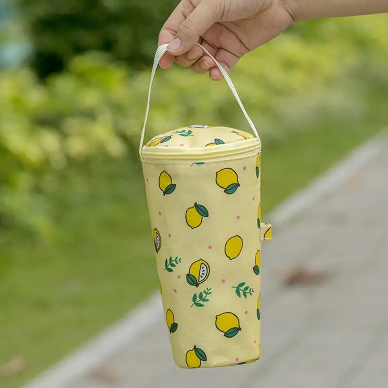 Yellow cylindrical bag with lemon pattern held by a hand outdoors