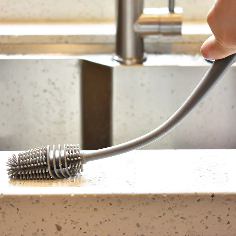 Gray kitchen brush with bristle head on a countertop next to a faucet.