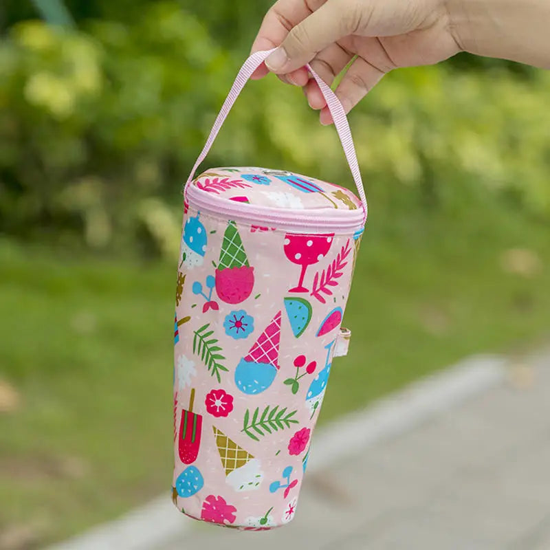 Colorful insulated bottle bag with a handle held by a hand outdoors.