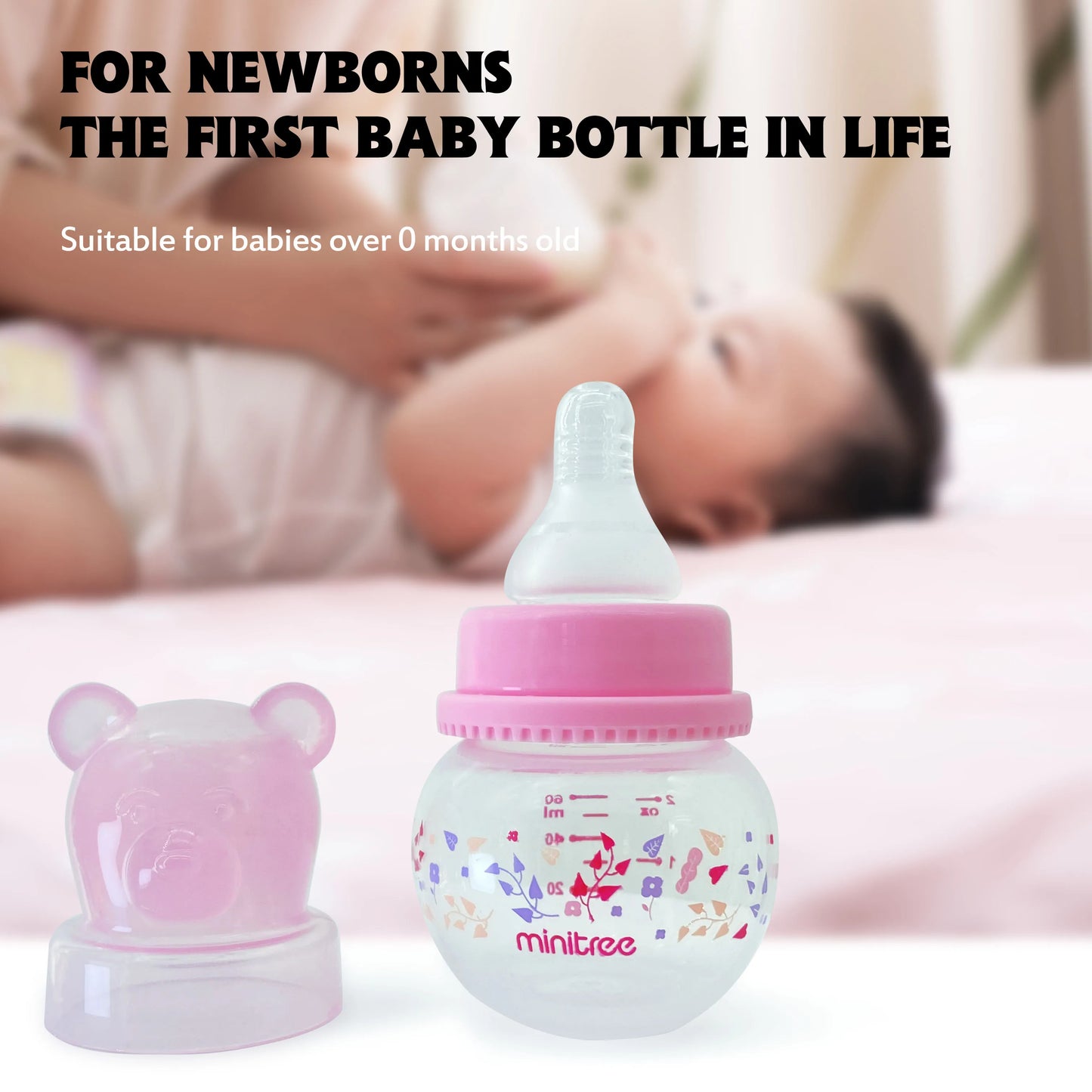 Baby bottle with pink cap and teddy bear design next to a baby lying down, suitable for newborns.