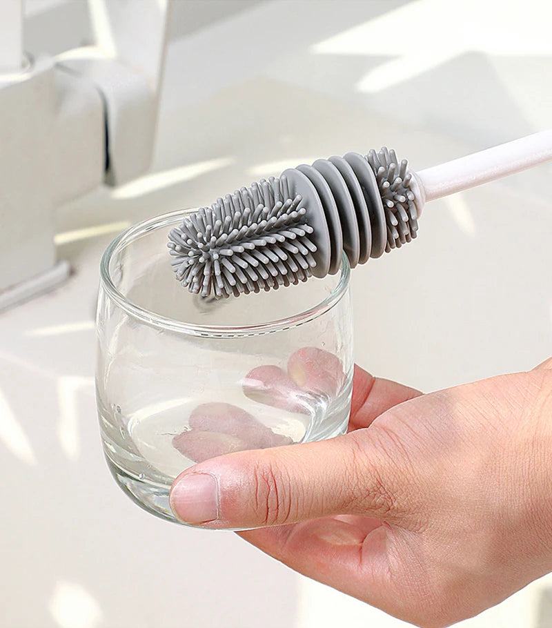 Person using a silicone bottle cleaning brush with a glass on a light background
