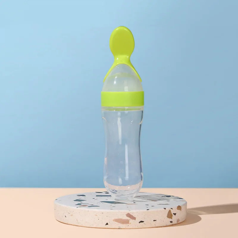 Clear baby bottle with green cap on a terrazzo coaster against a blue background