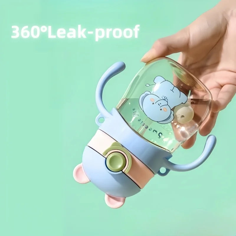 Children's sippy cup with cartoon design held by a hand on a light green background