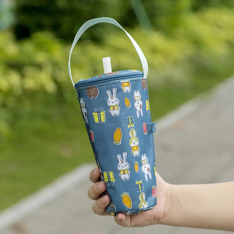 Blue insulated bottle bag with cartoon designs held by a hand outdoors.