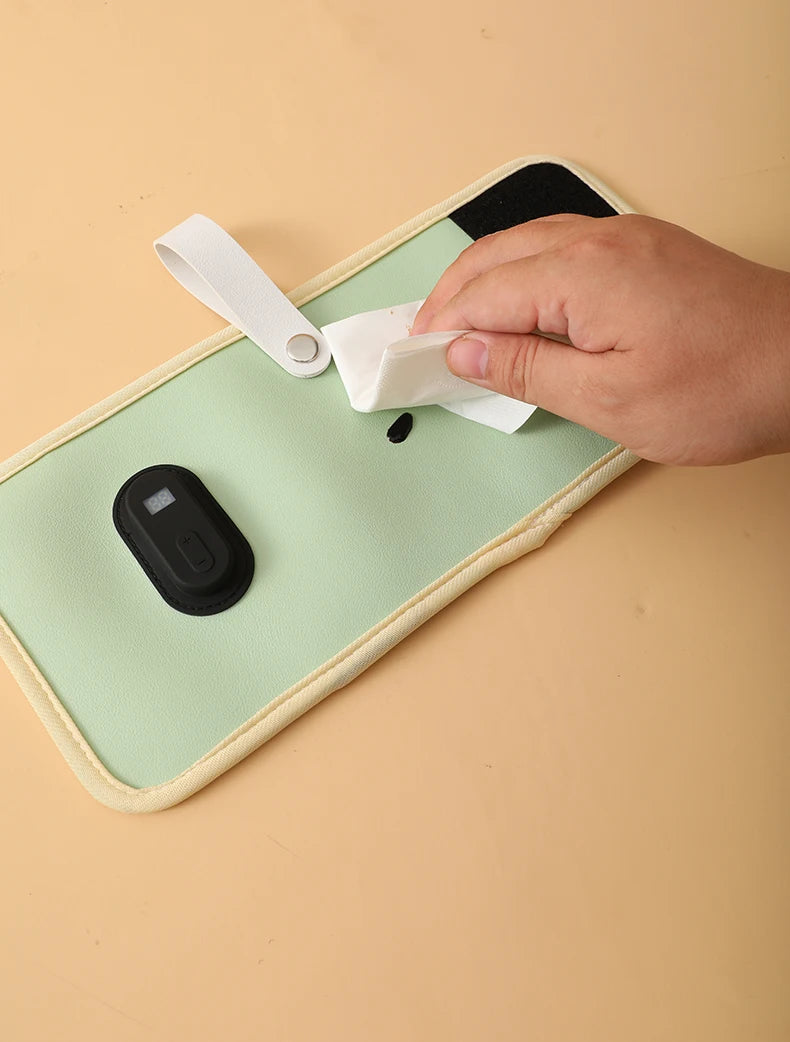 Hand cleaning a computer mouse with a wipe on a green mouse pad.