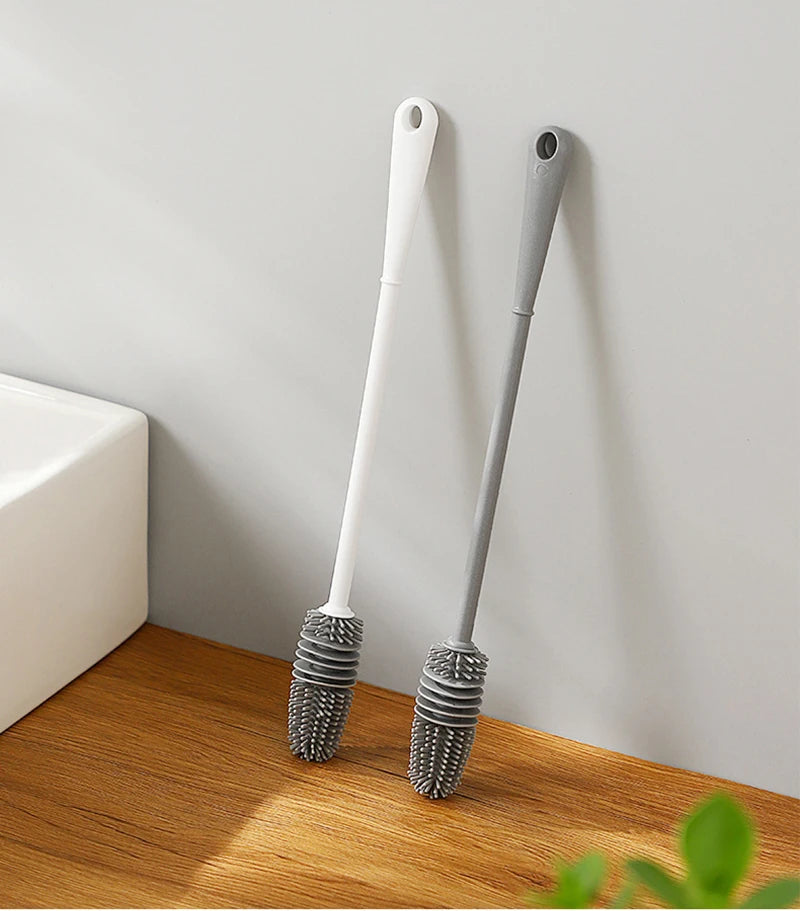 Two cleaning brushes with scrubber heads on a wooden surface against a white wall.