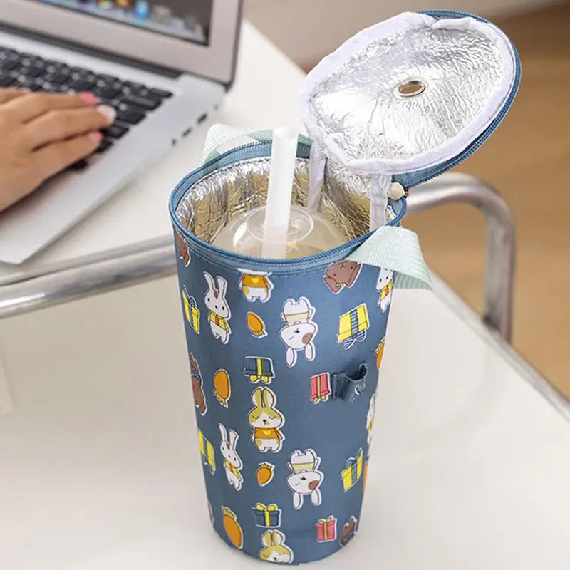 Insulated cup holder with cartoon designs on a desk next to a laptop.