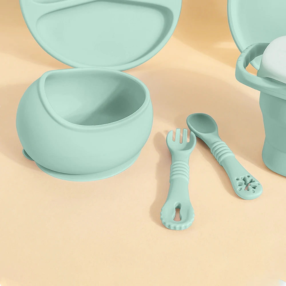 Mint green baby feeding set including bowl, spoon, and fork on a beige background