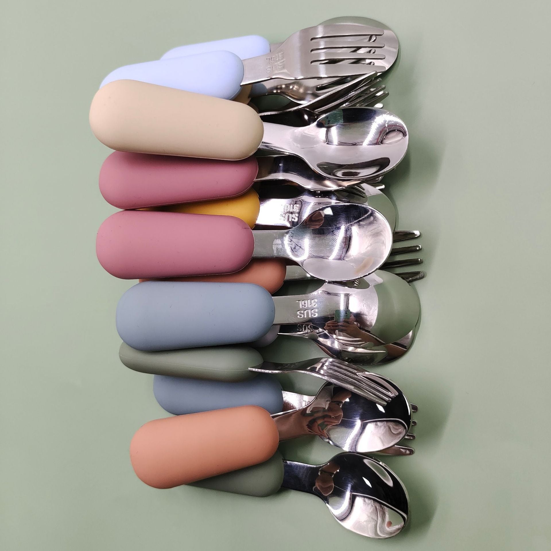 Set of silver cutlery with colorful handles on a light green background