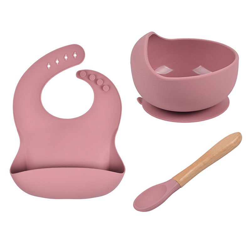 Pink baby bib, bowl, and spoon set on a white background