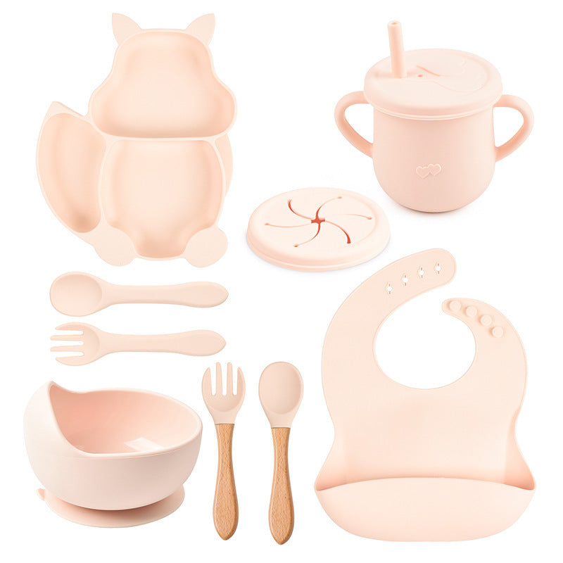 Beige silicone baby utensil set including bowl, spoon, fork, cup, and bib on a white background