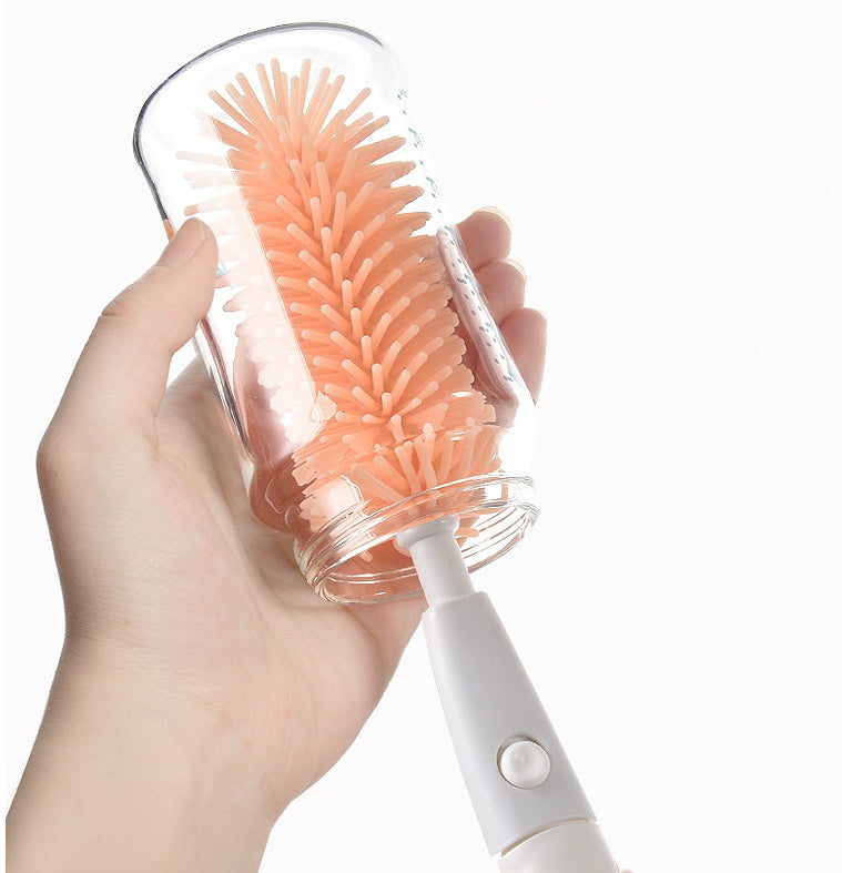Hand holding a bottle brush with a clear handle and coral bristles on a white background