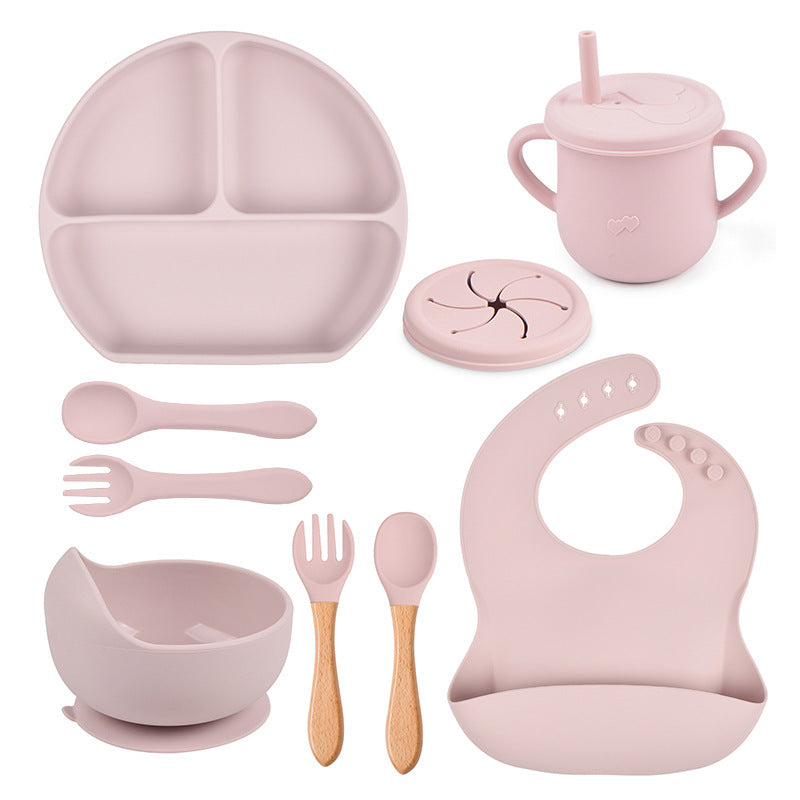 Pink children's dining set including a plate, cup, bowl, utensils, and bib on a white background.