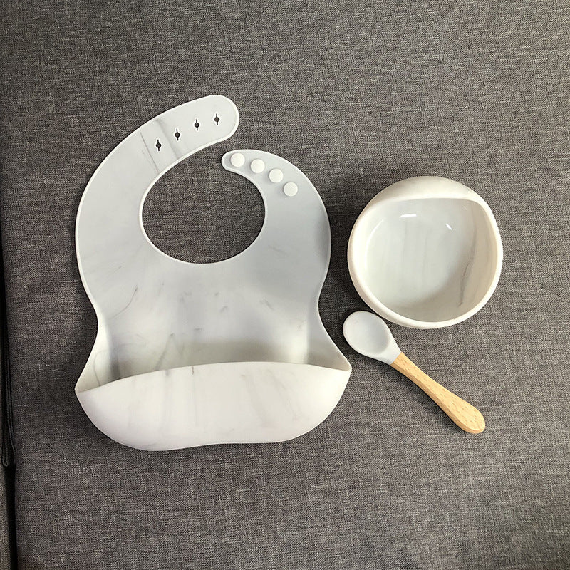 White silicone bib, bowl, and spoon on a gray textured background