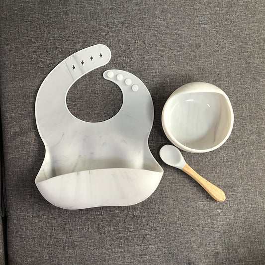 White silicone bib, bowl, and spoon on a gray textured background