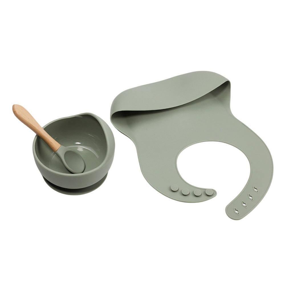 Green baby bowl with wooden spoon and matching bib on a white background