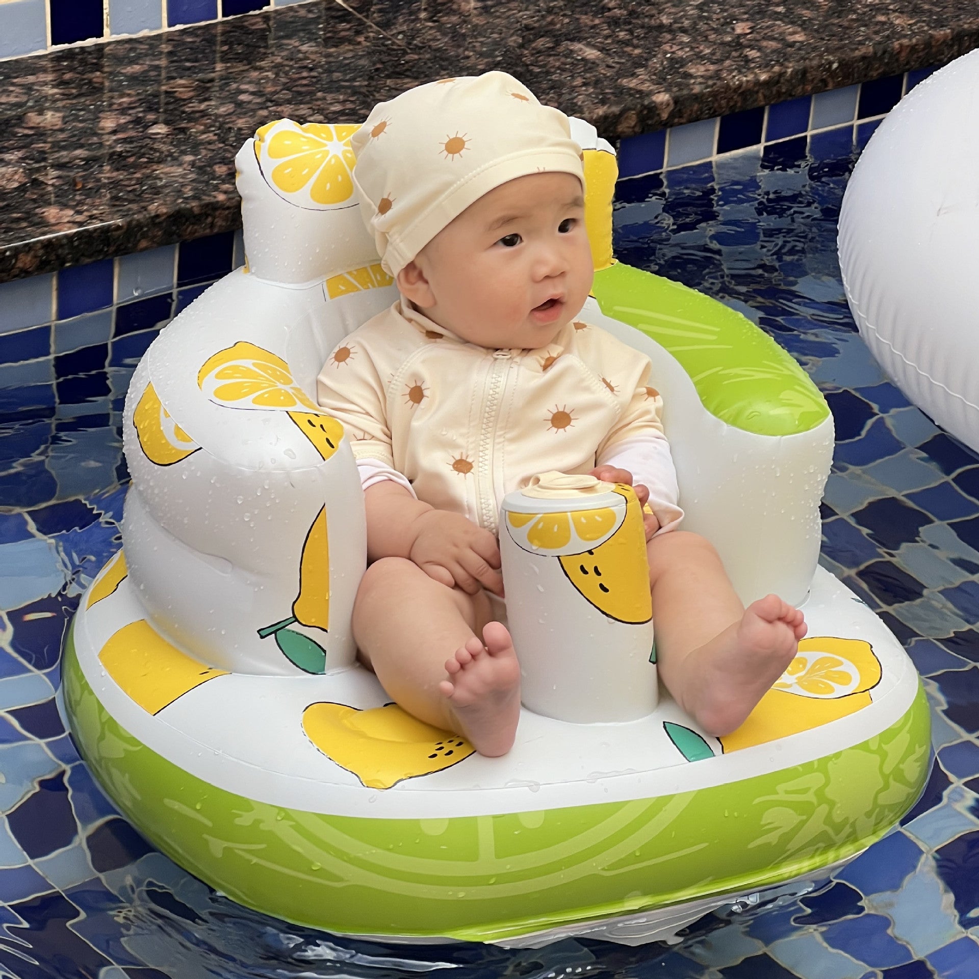 Baby sitting in a lemon-themed inflatable seat by a pool.