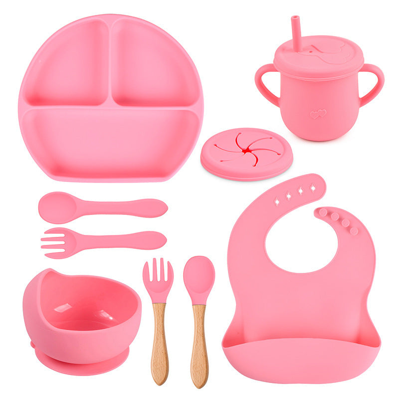 Pink children's dining set including plate, cup, bowl, utensils, and bib on a white background
