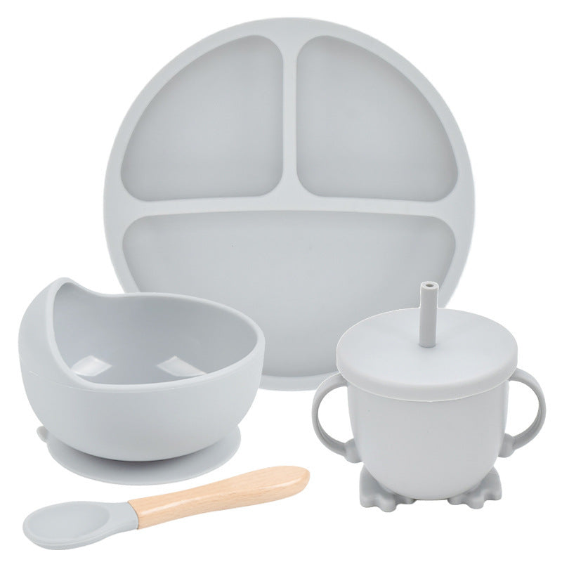 Set of gray silicone dining utensils including a plate, bowl, cup with straw, and spoon on a white background.