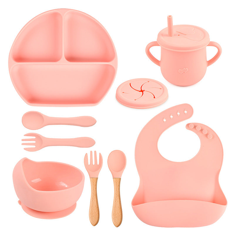 Pink children's dining set including a plate, cup, bowl, utensils, and bib on a white background.