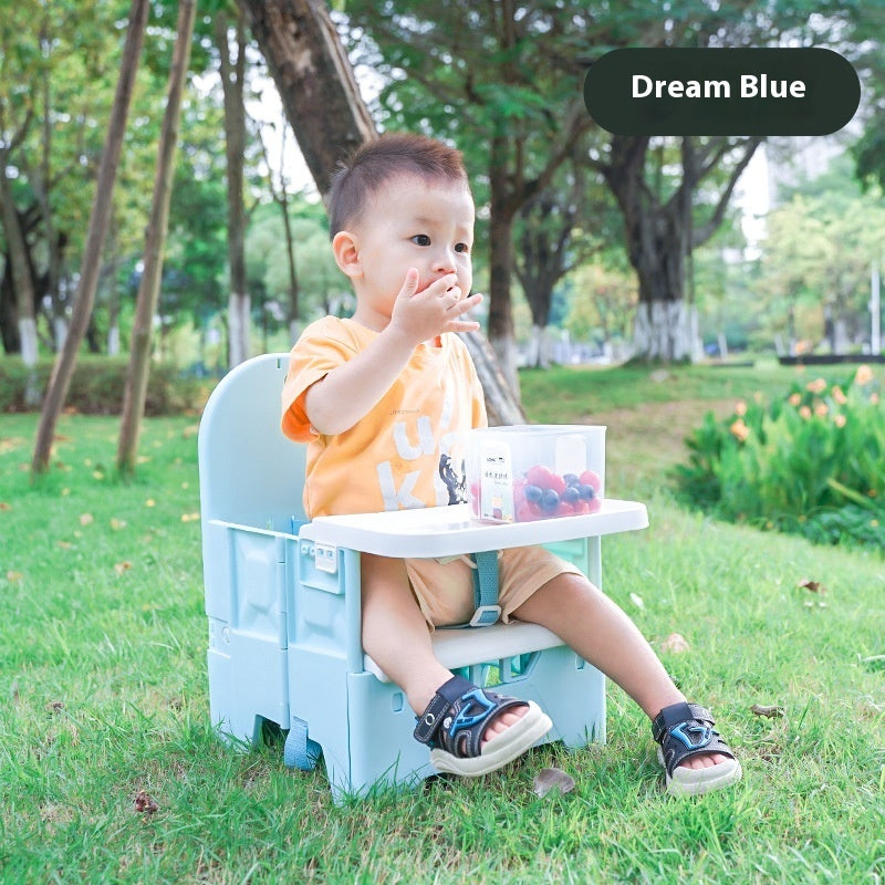 Child sitting on a blue and white chair with a small table in a park, eating berries.