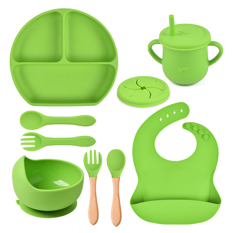 Green silicone dining set including plate, cup, bowl, utensils, and bib on a white background