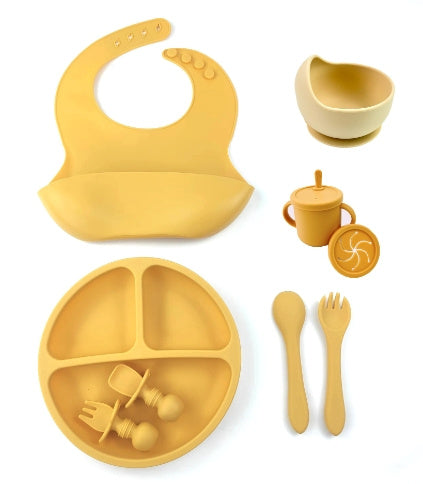 Yellow silicone baby feeding set including bib, plate, cup, and utensils on a white background