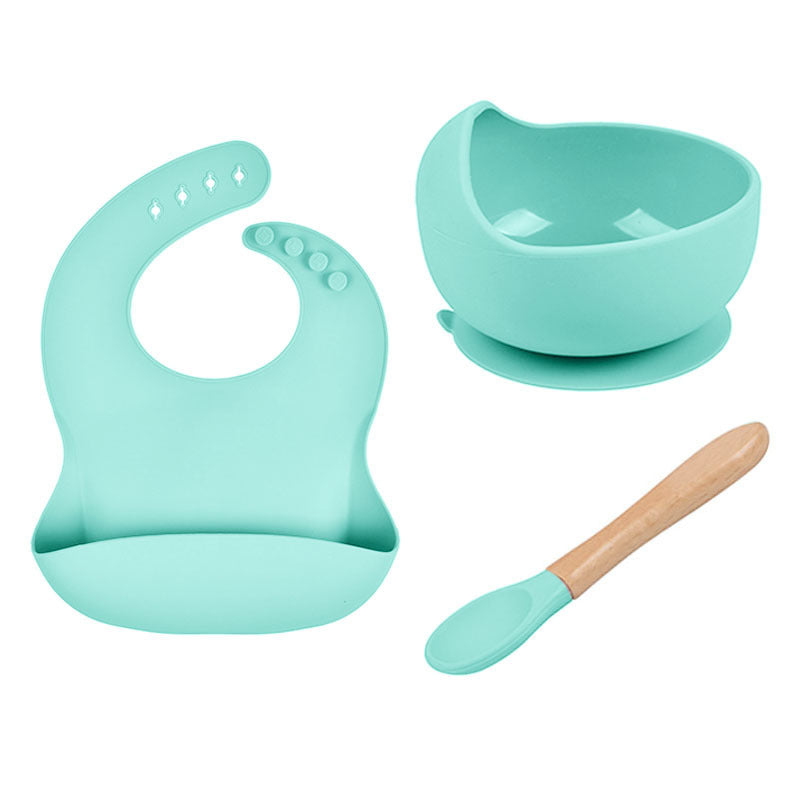 Set of turquoise baby bib, bowl with suction cup, and wooden spoon on a white background