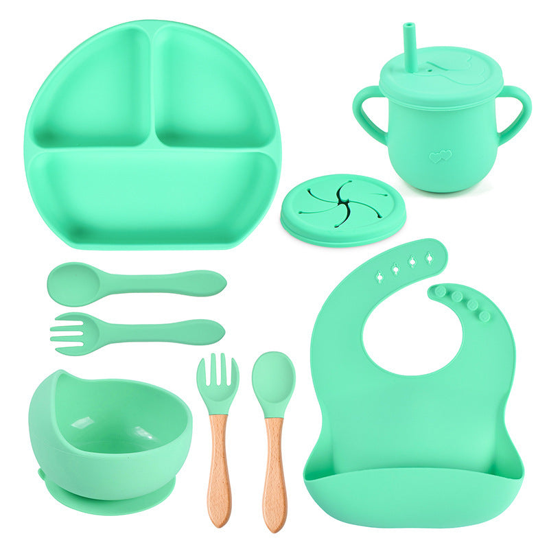 Set of green baby吃饭 utensils including plate, cup, bowl, spoons, forks, and bib on a white background.